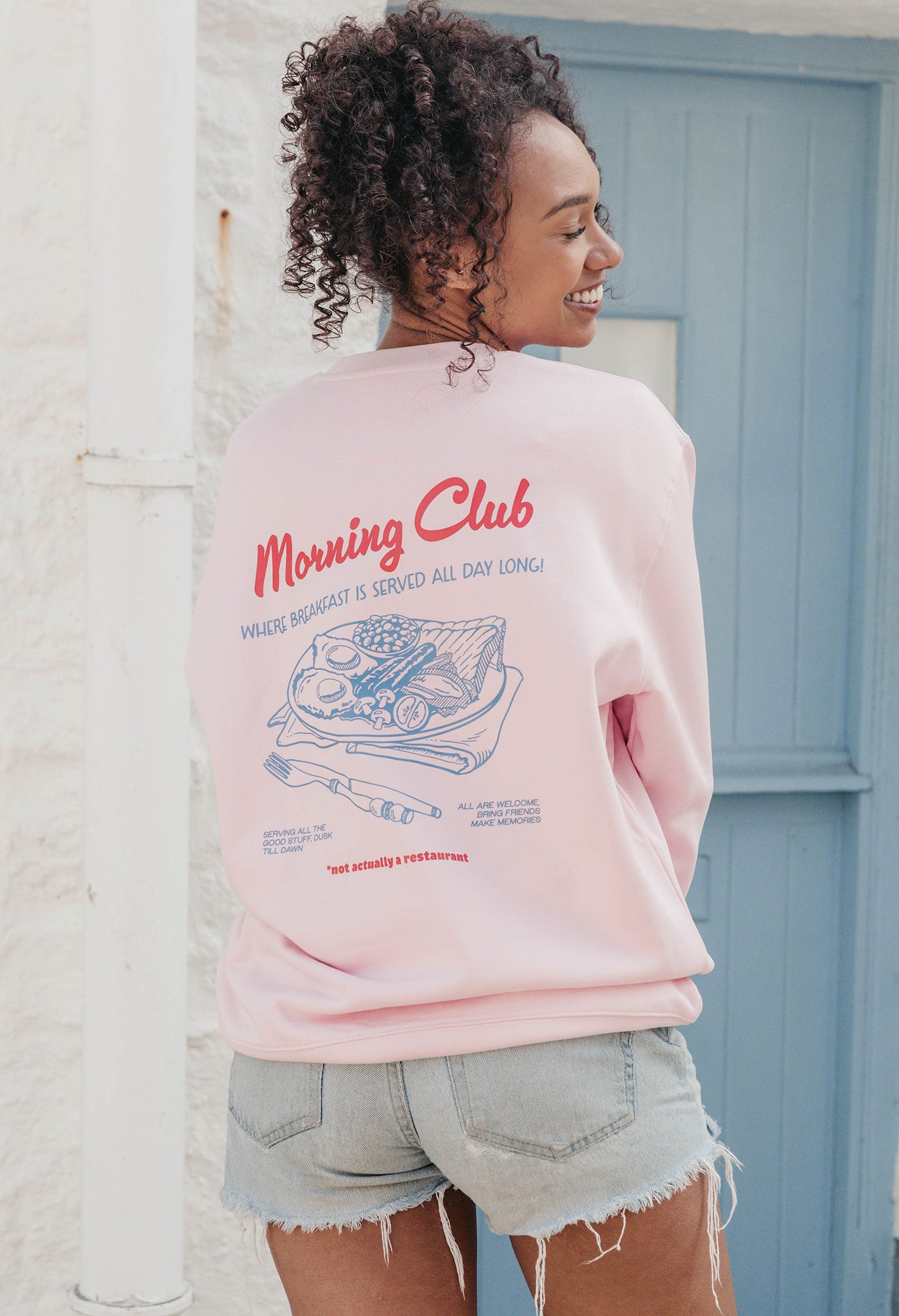 A lady wearing a printed breakfast fry-up graphic style sweatshirt, set by the sea.