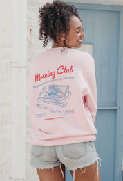 A lady wearing a printed breakfast fry-up graphic style sweatshirt, set by the sea.