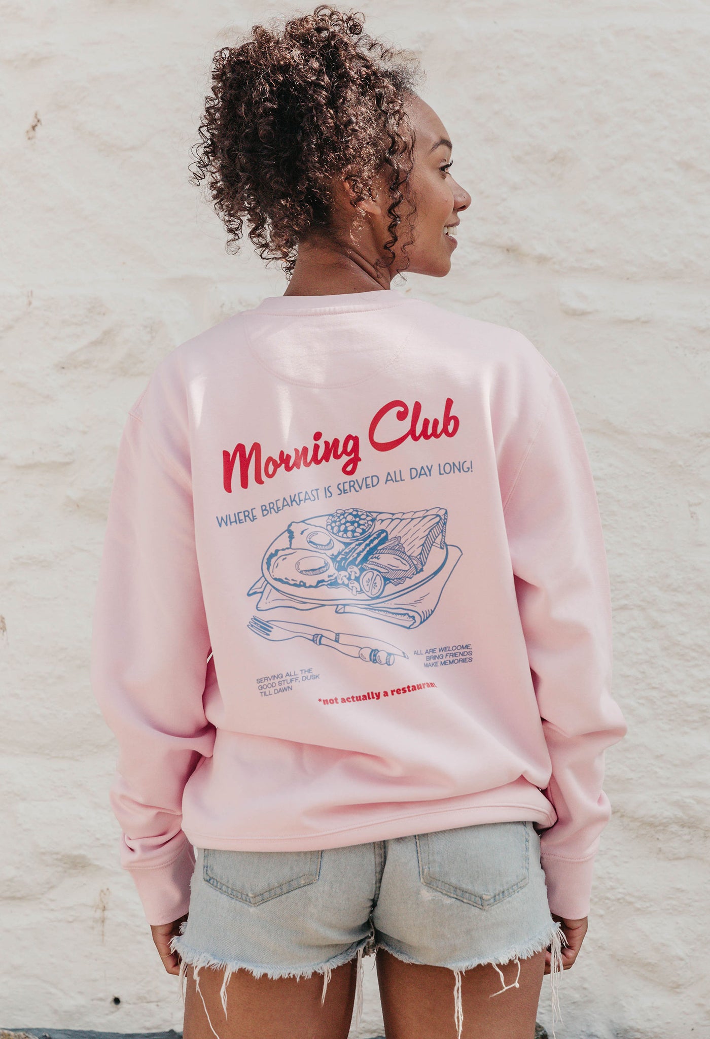 A lady wearing a printed breakfast fry-up graphic style sweatshirt, set by the sea.