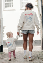 A lady wearing a printed breakfast fry-up graphic style sweatshirt, set by the sea.