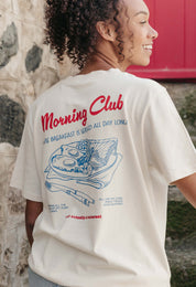 A lady wearing a natural printed graphic t-shirt, with a illustration of a breakfast fry up, set in a town.