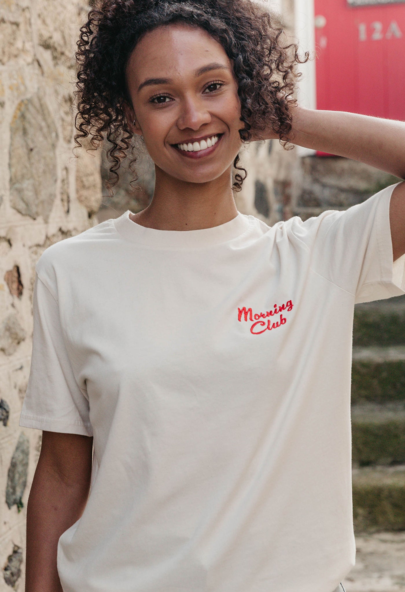 A lady wearing a natural printed graphic t-shirt, with a illustration of a breakfast fry up, set in a town.