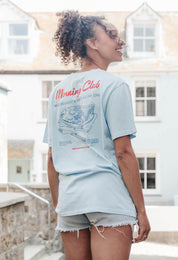 A lady wearing a blue printed graphic t-shirt, with a illustration of a breakfast fry up, set in a town.