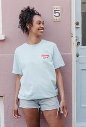 A lady wearing a blue printed graphic t-shirt, with a illustration of a breakfast fry up, set in a town.