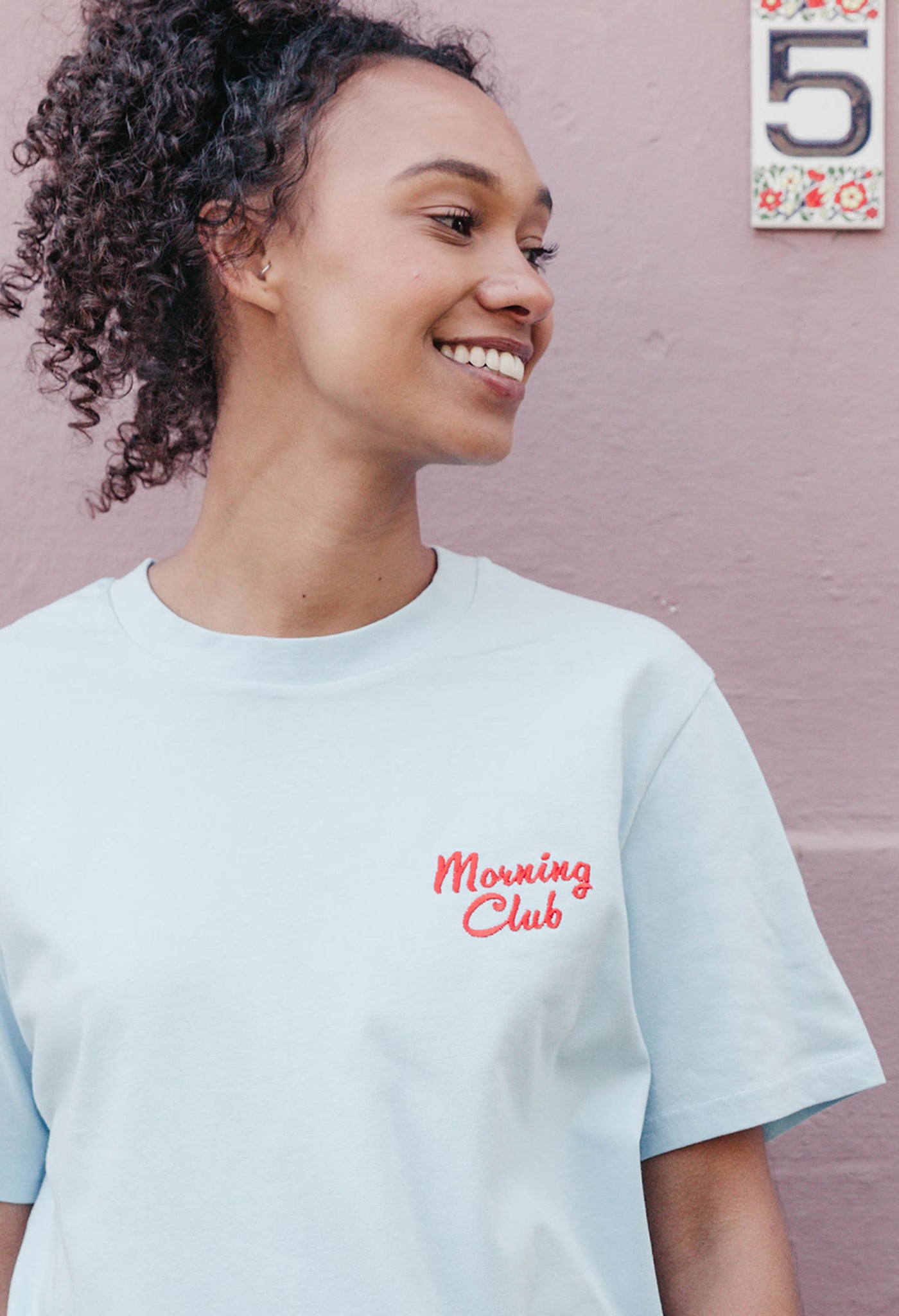 A lady wearing a blue printed graphic t-shirt, with a illustration of a breakfast fry up, set in a town.