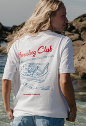 A lady wearing a white printed graphic t-shirt, with a illustration of a breakfast fry up, set in a town.