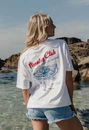 A lady wearing a white printed graphic t-shirt, with a illustration of a breakfast fry up, set in a town.