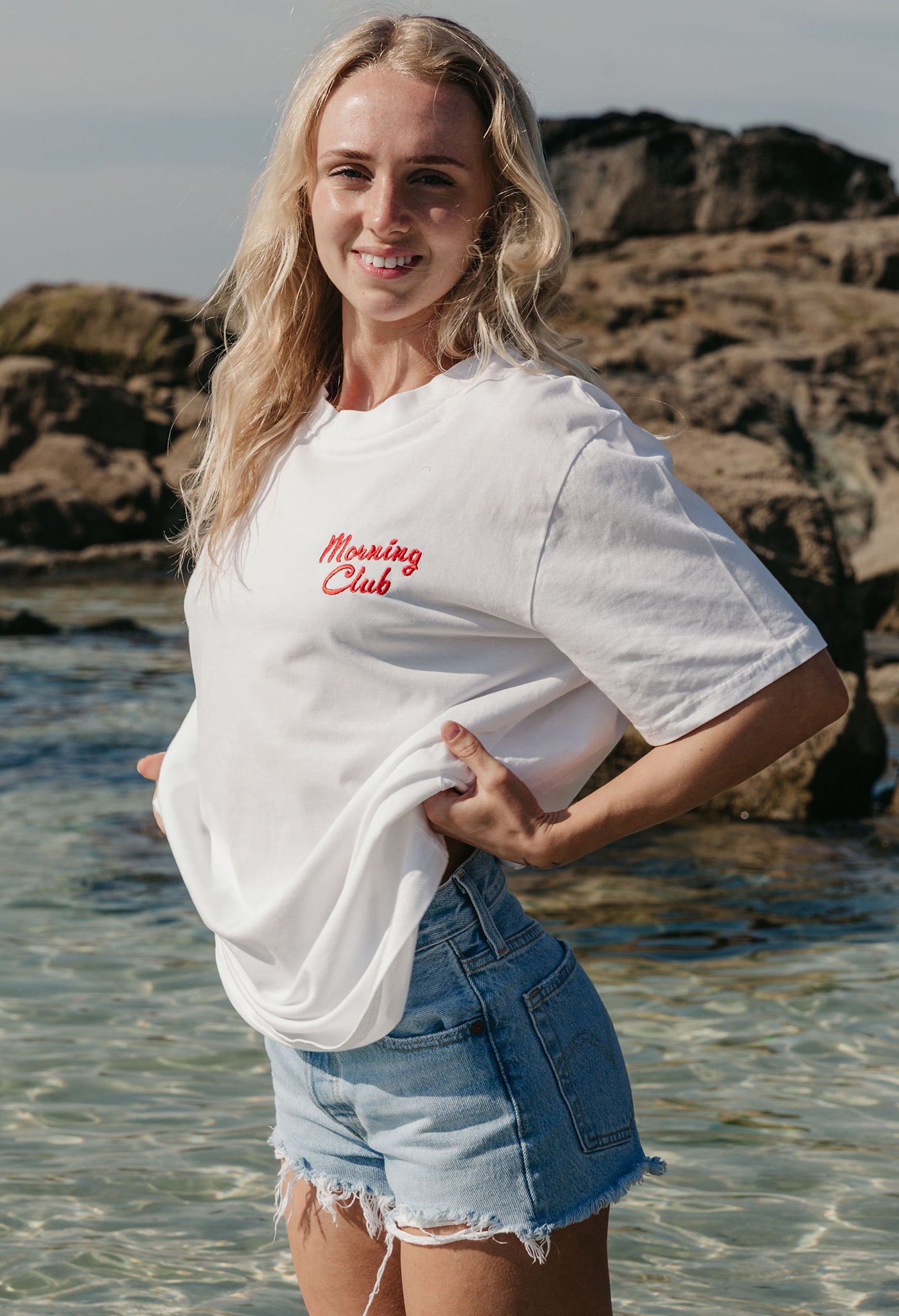 A lady wearing a white printed graphic t-shirt, with a illustration of a breakfast fry up, set in a town.