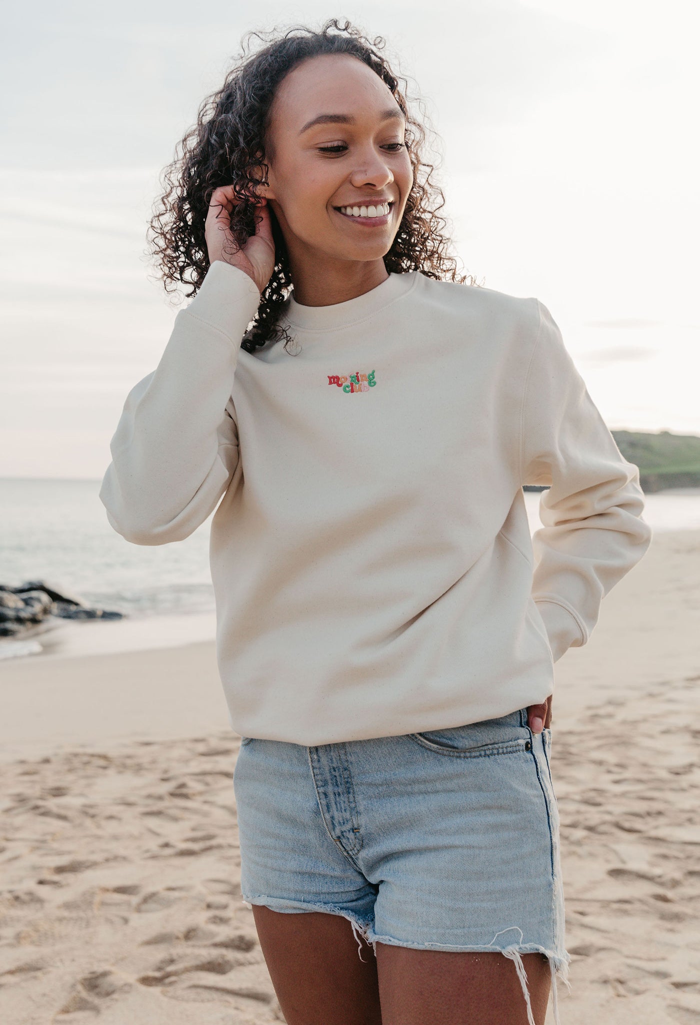 Lady wearing a plain embroidered sweatshirt, and its set on the beach.