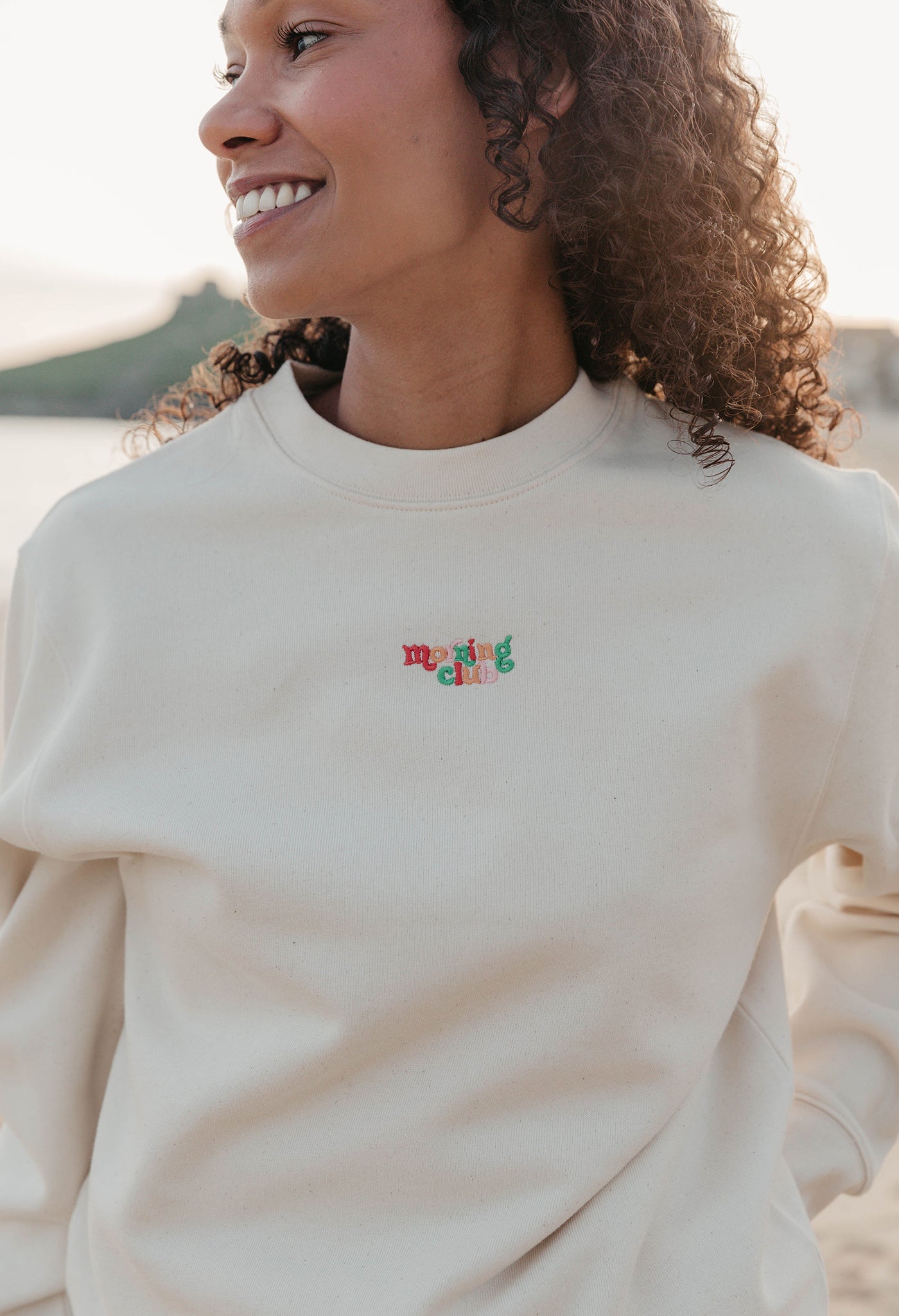 Lady wearing a plain embroidered sweatshirt, and its set on the beach.