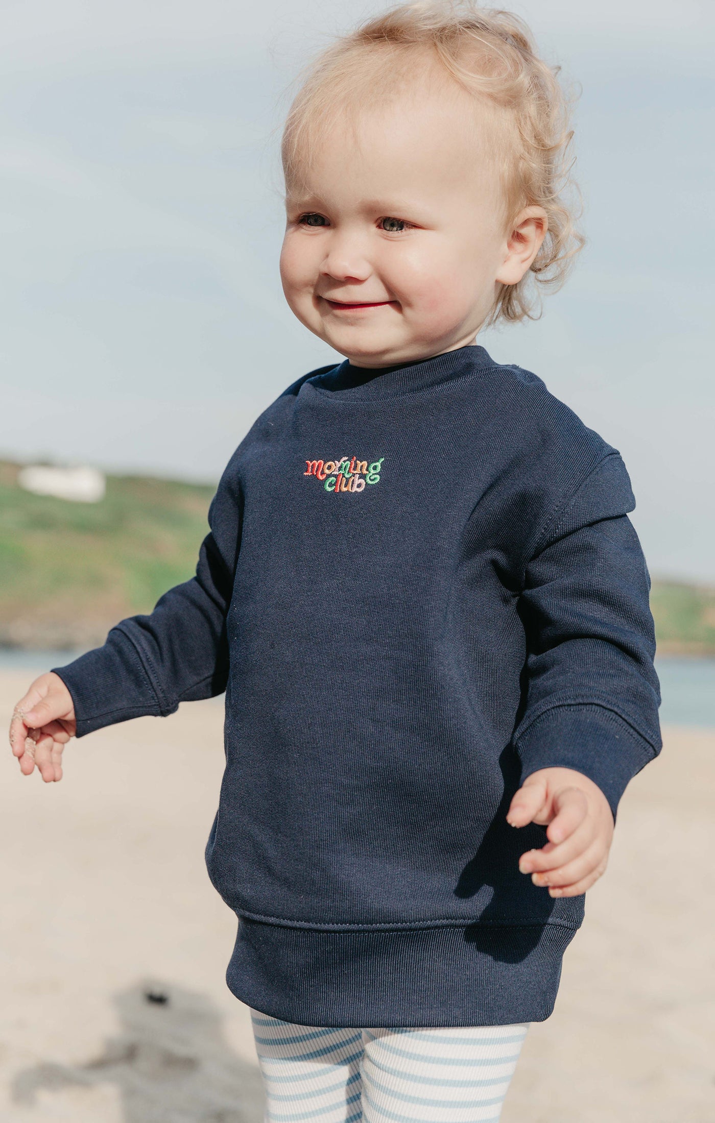 Toddler wearing a plain embroidered sweatshirt, that says morning club.