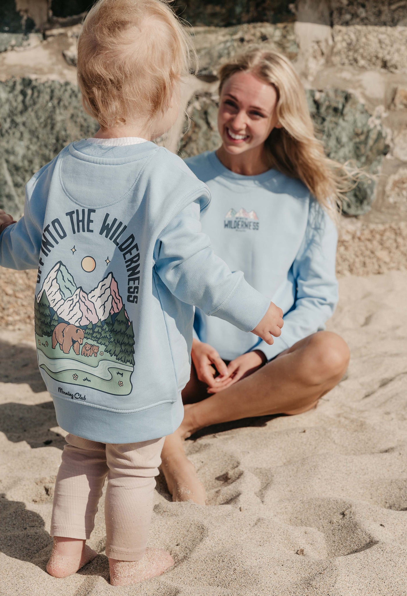 Lady wearing a printed sweatshirt, that says into the wilderness, and its set on the beach.