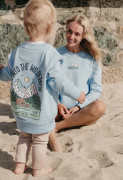 Lady wearing a printed sweatshirt, that says into the wilderness, and its set on the beach.