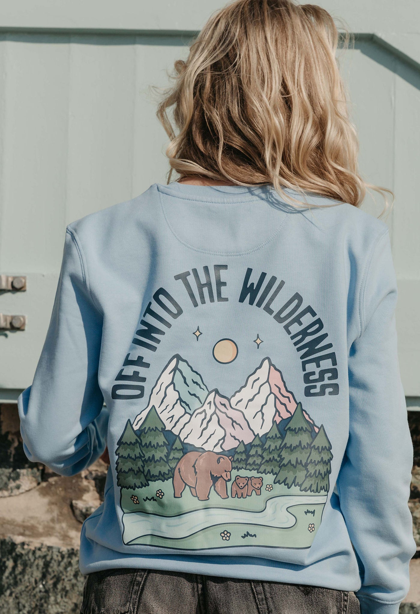 Lady wearing a printed sweatshirt, that says into the wilderness, and its set on the beach.