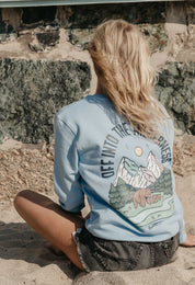 Lady wearing a printed sweatshirt, that says into the wilderness, and its set on the beach.