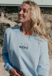 Lady wearing a printed sweatshirt, that says into the wilderness, and its set on the beach.