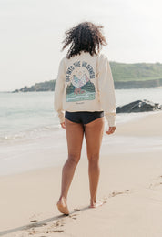 Lady wearing a printed sweatshirt, that says into the wilderness, and its set on the beach.