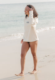 Lady wearing a printed sweatshirt, that says into the wilderness, and its set on the beach.