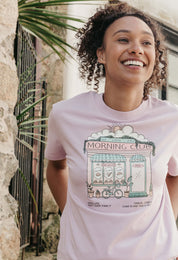 A lady wearing a lilac printed graphic t-shirt, Morning Club Cafe, set in a town.