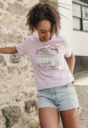 A lady wearing a lilac printed graphic t-shirt, Morning Club Cafe, set in a town.