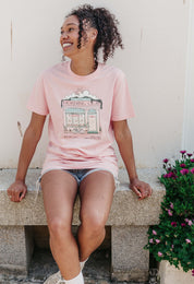 A lady wearing a pink printed graphic t-shirt, Morning Club Cafe, set in a town.