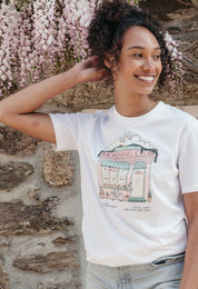 A lady wearing a white printed graphic t-shirt, Morning Club Cafe, set in a town.