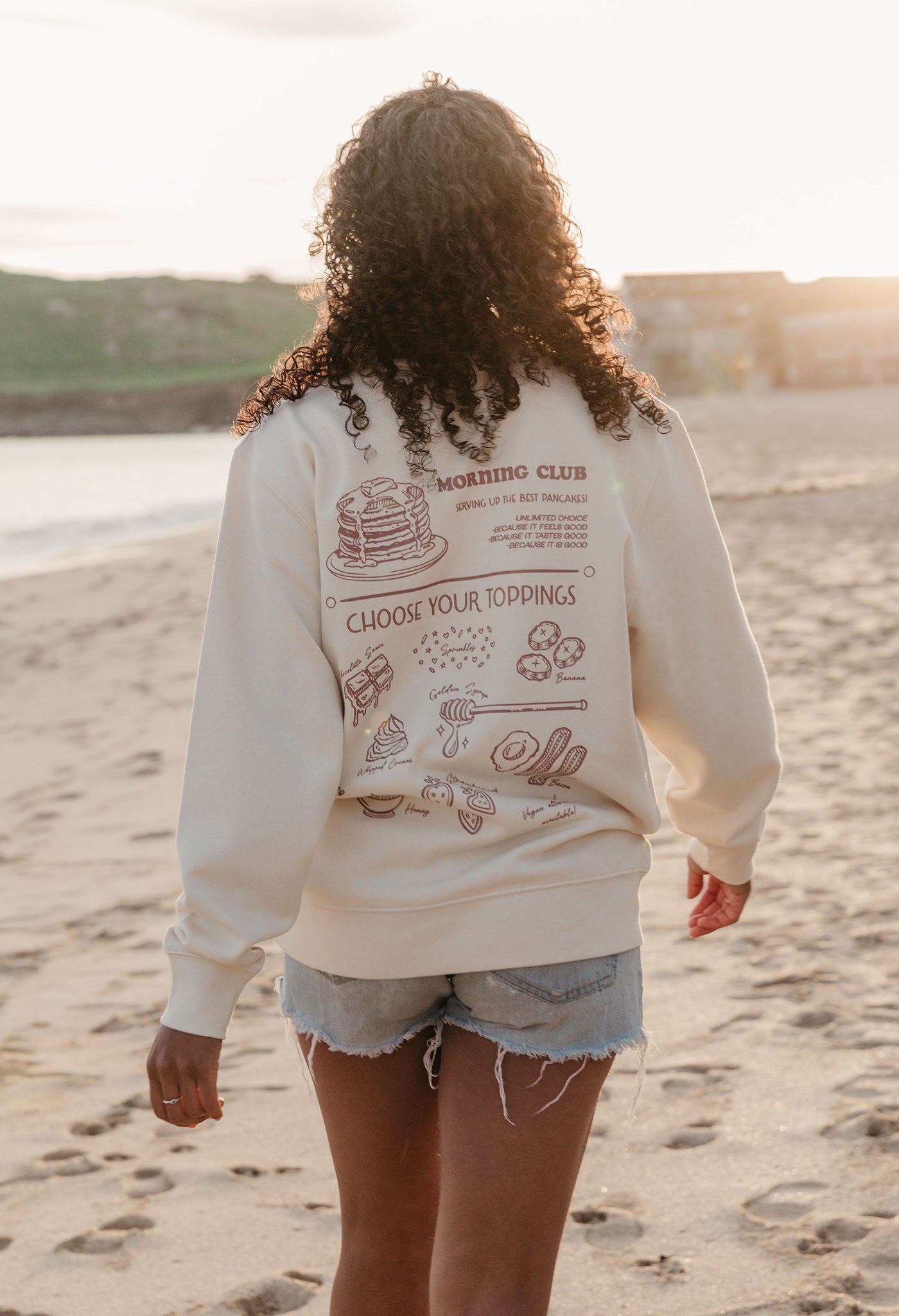 A lady wearing a printed pancake style printed sweatshirt, set by the sea.