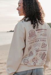 A lady wearing a printed pancake style printed sweatshirt, set by the sea.