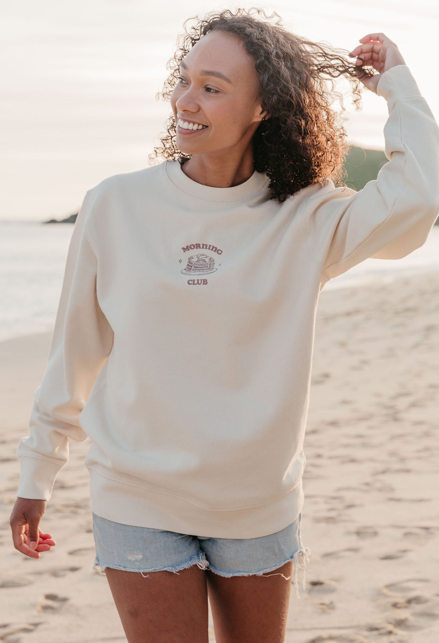 A lady wearing a printed pancake style printed sweatshirt, set by the sea.