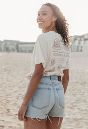 A lady wearing a natural printed graphic t-shirt, with a illustration of a pancakes and toppings.