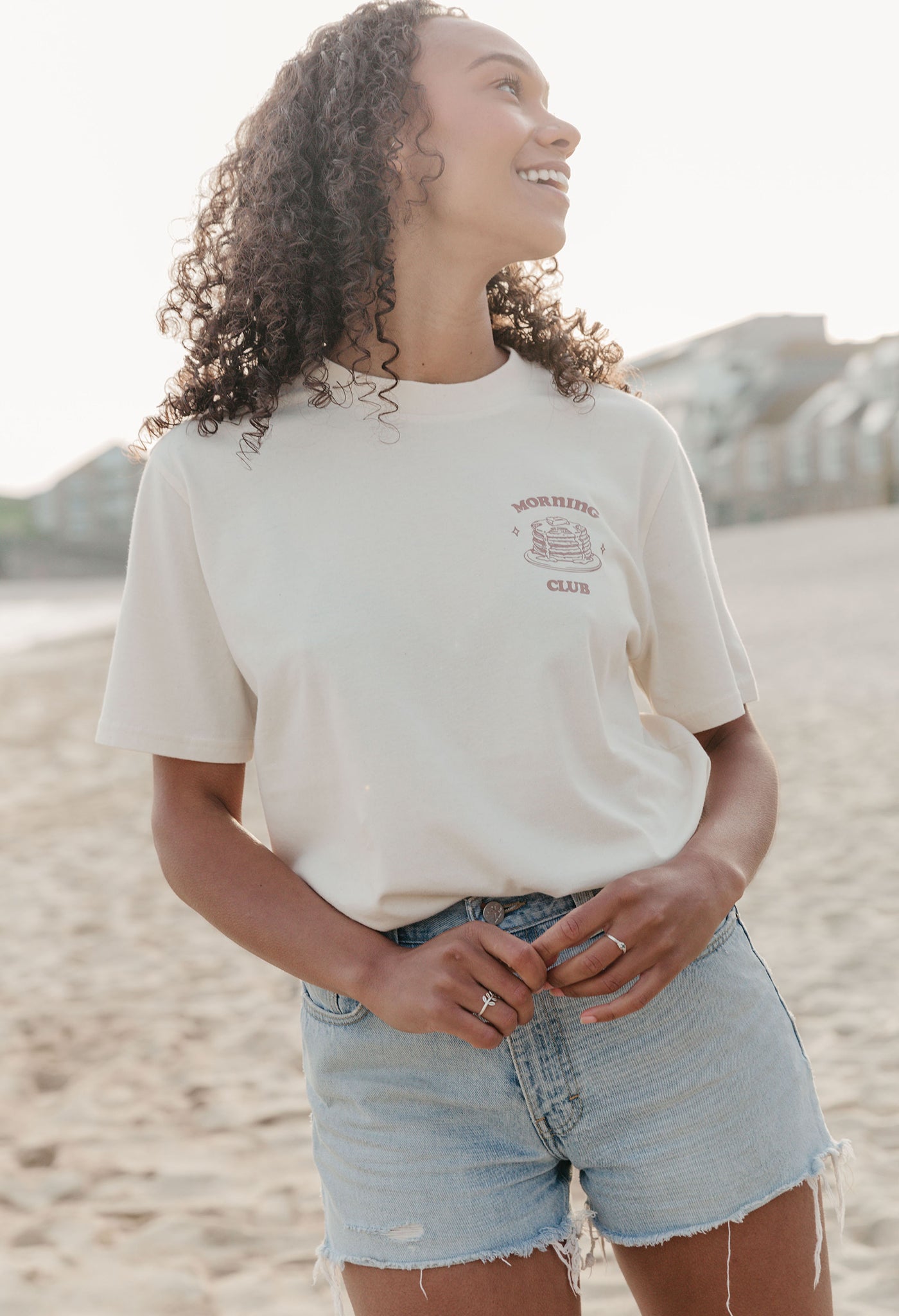 A lady wearing a natural printed graphic t-shirt, with a illustration of a pancakes and toppings.