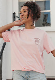 A lady wearing a pink printed graphic t-shirt, with a illustration of a pancakes and toppings.