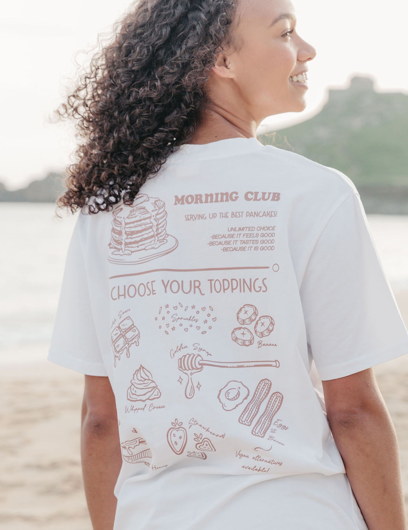 A lady wearing a white printed graphic t-shirt, with a illustration of a pancakes and toppings.