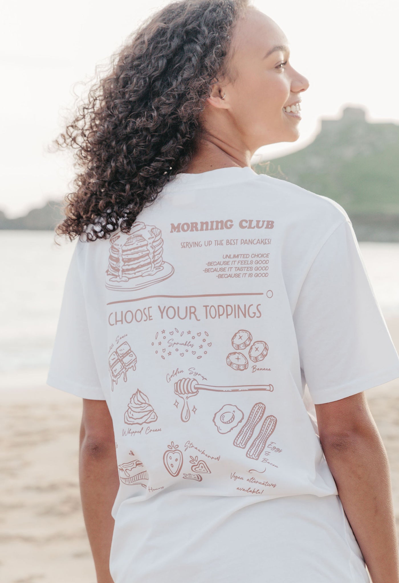 A lady wearing a white printed graphic t-shirt, with a illustration of a pancakes and toppings.