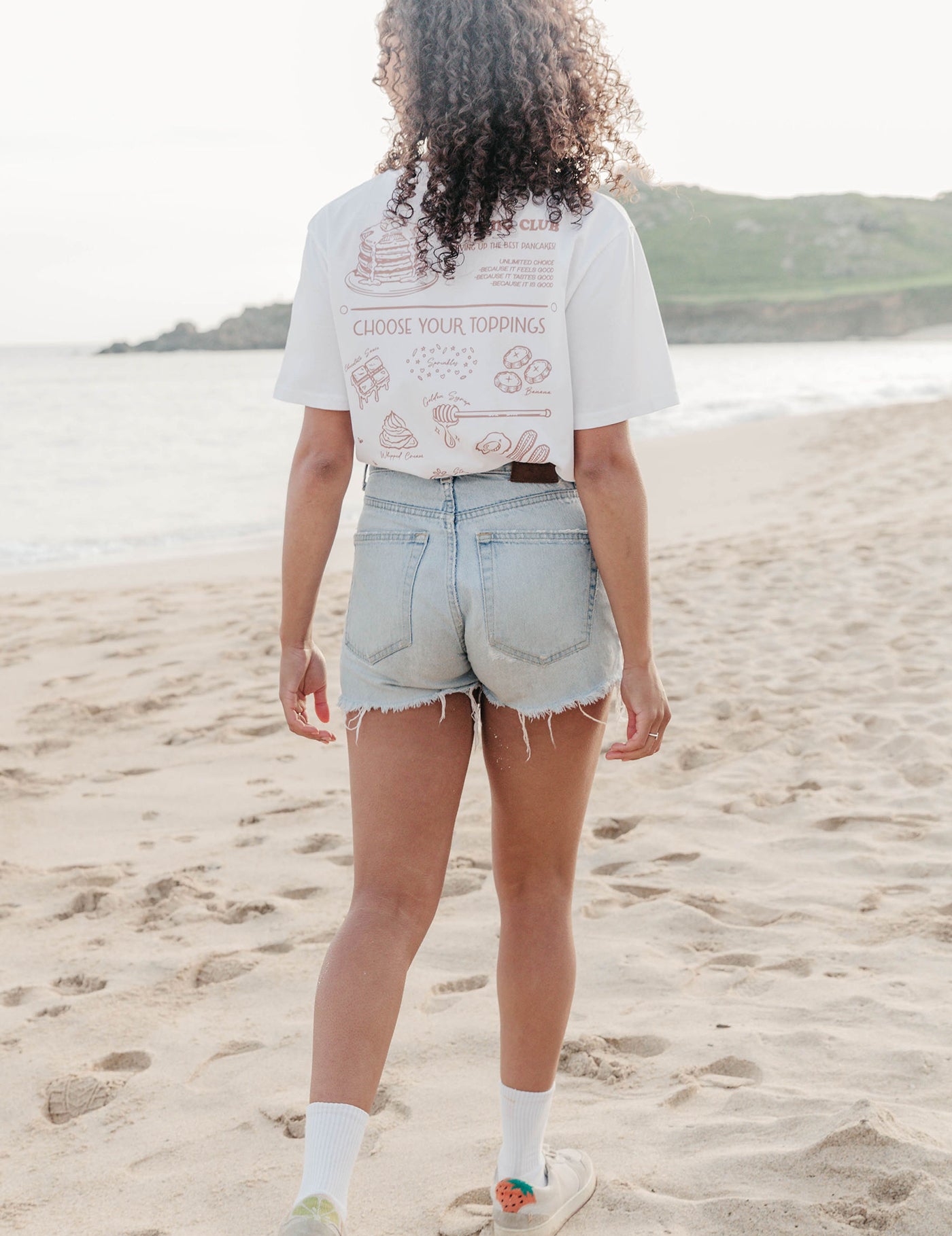 A lady wearing a white printed graphic t-shirt, with a illustration of a pancakes and toppings.