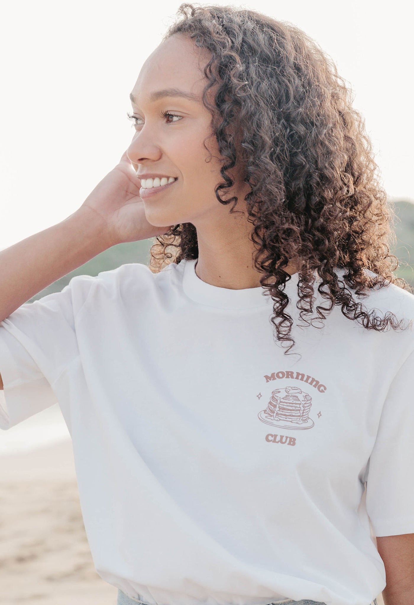 A lady wearing a white printed graphic t-shirt, with a illustration of a pancakes and toppings.