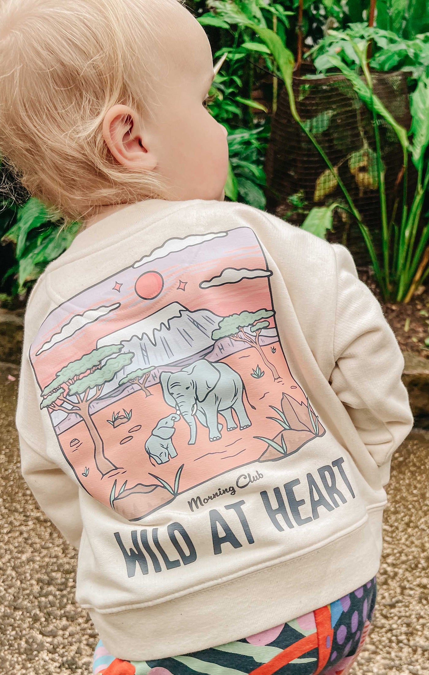 Toddler wearing a printed sweatshirt, that says wild at heart, featuring an elephant print.