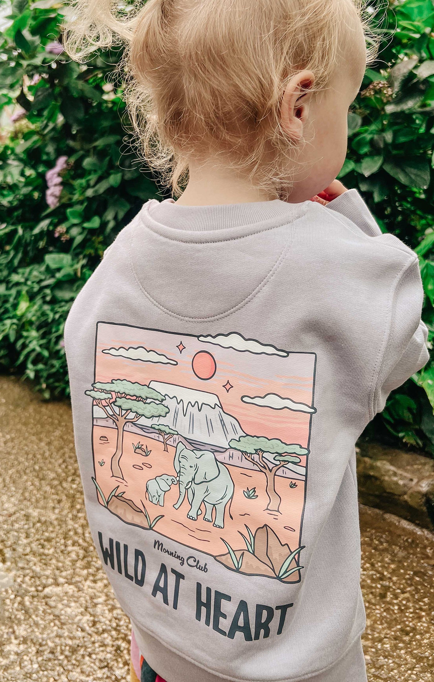 Toddler wearing a printed sweatshirt, that says wild at heart, featuring an elephant print.