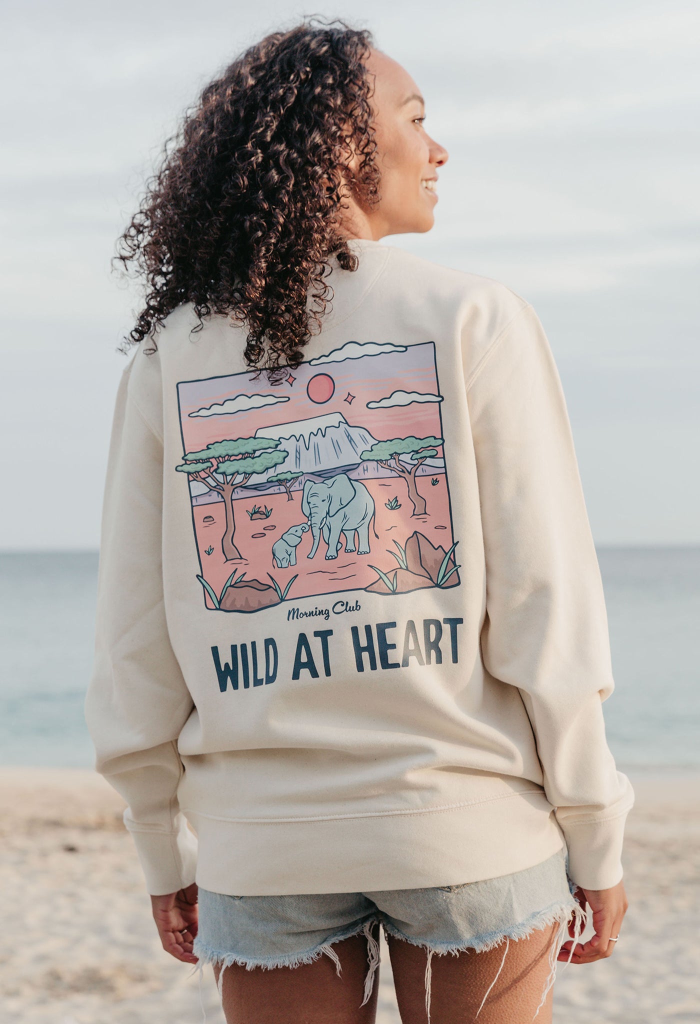 Lady wearing a printed sweatshirt, that says wild at heart, and its set on the beach.