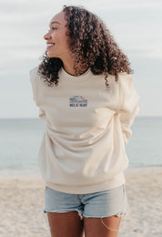 Lady wearing a printed sweatshirt, that says wild at heart, and its set on the beach.