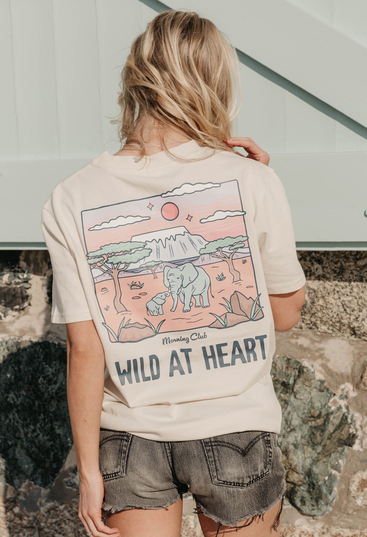 A lady wearing a natural printed graphic t-shirt, that says wild at heart, set by the beach.