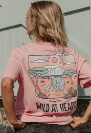 A lady wearing a pink printed graphic t-shirt, that says wild at heart, set by the beach.