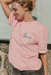 A lady wearing a pink printed graphic t-shirt, that says wild at heart, set by the beach.